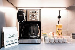 Eine Kaffeemaschine, eine Packung Quills-Kaffee und ein Spender für französischen Vanillesirup auf einer Küchenarbeitsplatte.