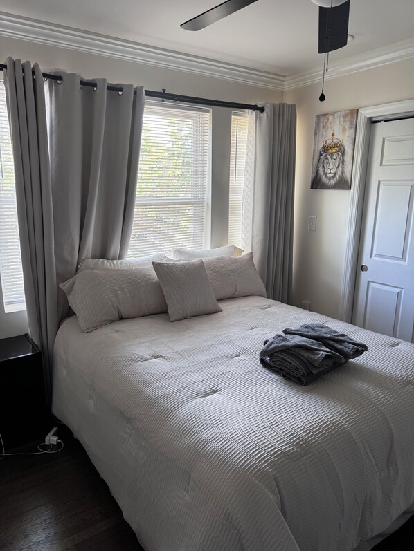 Un dormitorio con cama, cortinas, un cuadro y una puerta.