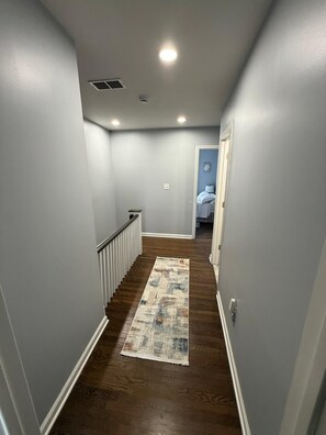 Un pasillo con piso de madera, paredes blancas y un tapete estampado.