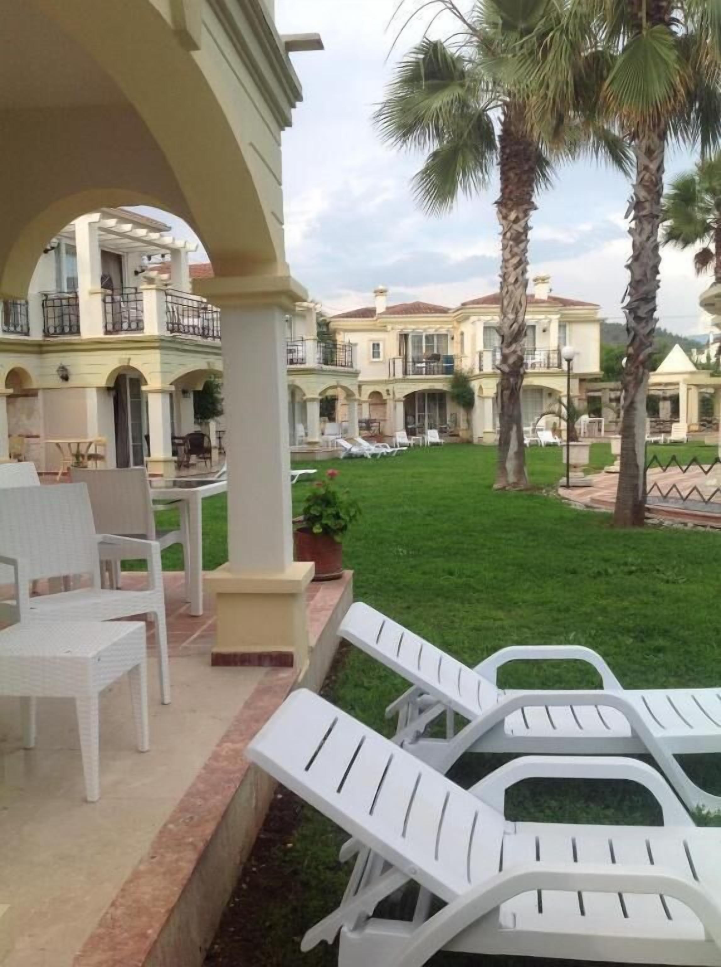 A courtyard with white lounge chairs, a covered seating area, and a well-maintained lawn.