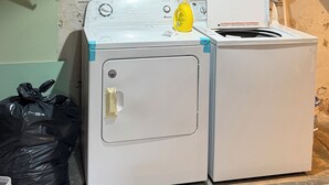 Un lavadero con dos lavadoras, una botella de detergente amarillo y un tubo grande en el techo.