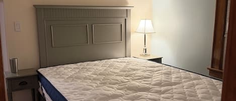 Un dormitorio con cama, mesita de noche, lámpara y armario de madera.