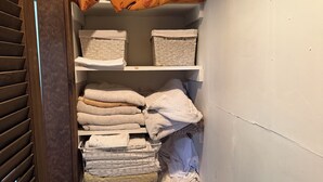 Un armario de almacenamiento con estantes que contienen toallas dobladas, una cesta y una caja de cartón.