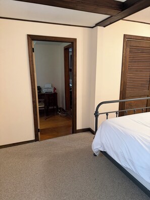A bedroom with a bed, a wooden door, and a carpeted floor.