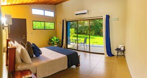 A bedroom with a bed, a small table, a potted plant, and a view of a garden through a sliding glass door. - 3 Bedroom Escape - 15 Min from La Fortuna (Provincia de Alajuela)