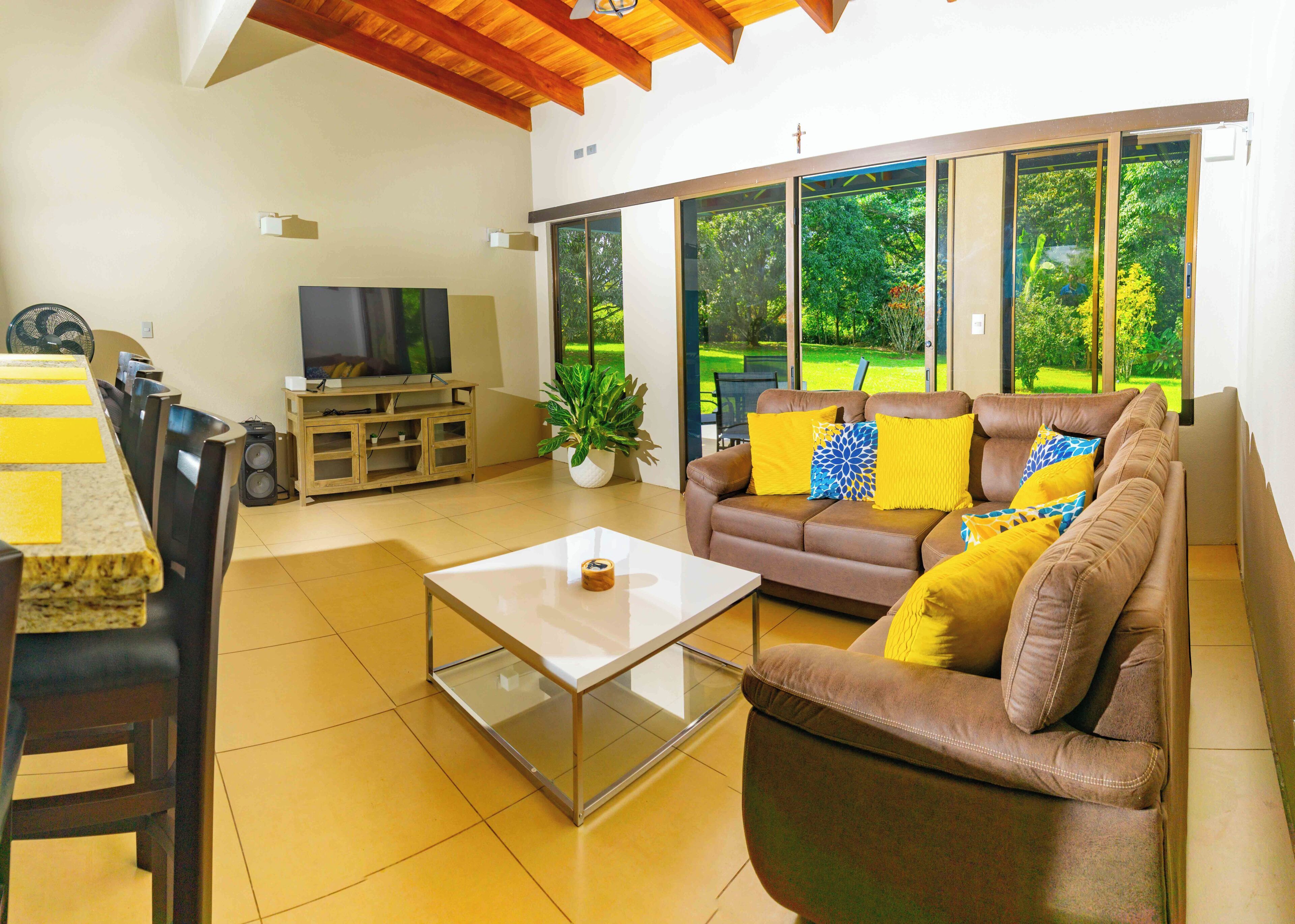 Ein Wohnzimmer mit einer Couch, einem Couchtisch, einem Fernseher und Blick auf einen Garten durch große Fenster.