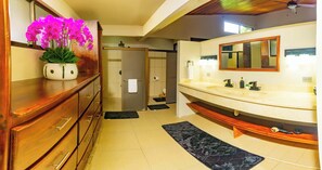 A modern bathroom with a wooden vanity, a large mirror, and a potted orchid.