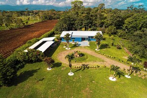 A modern two-story house with a blue exterior, surrounded by a well-maintained garden with various plants and a paved driveway. - 3 Bedroom Escape - 15 Min from La Fortuna (Provincia de Alajuela)