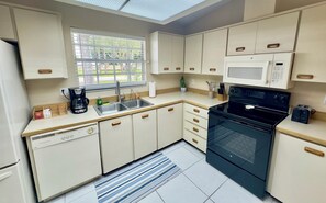A compact kitchen with a dishwasher, stove, microwave, and a window with blinds. - Coastal Charm, Chic Home Near The Beach! (Port Orange)