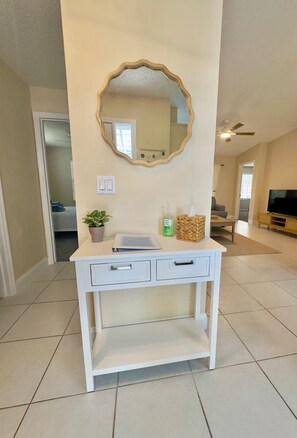 A white vanity with a mirror, two drawers, a shelf, a potted plant, and a bottle of hand soap. - Coastal Charm, Chic Home Near The Beach! (Port Orange)