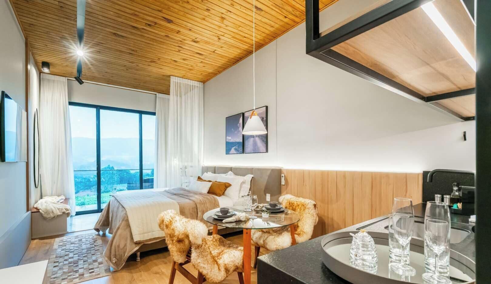 A hotel room with a bed, a dining table with chairs, a large window, and a view of the outdoors.