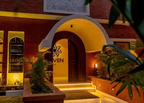 A hotel entrance with a brick facade, a yellow-lit archway, and a sign with the hotel's name. - 7EVEN Suites (Lagos)
