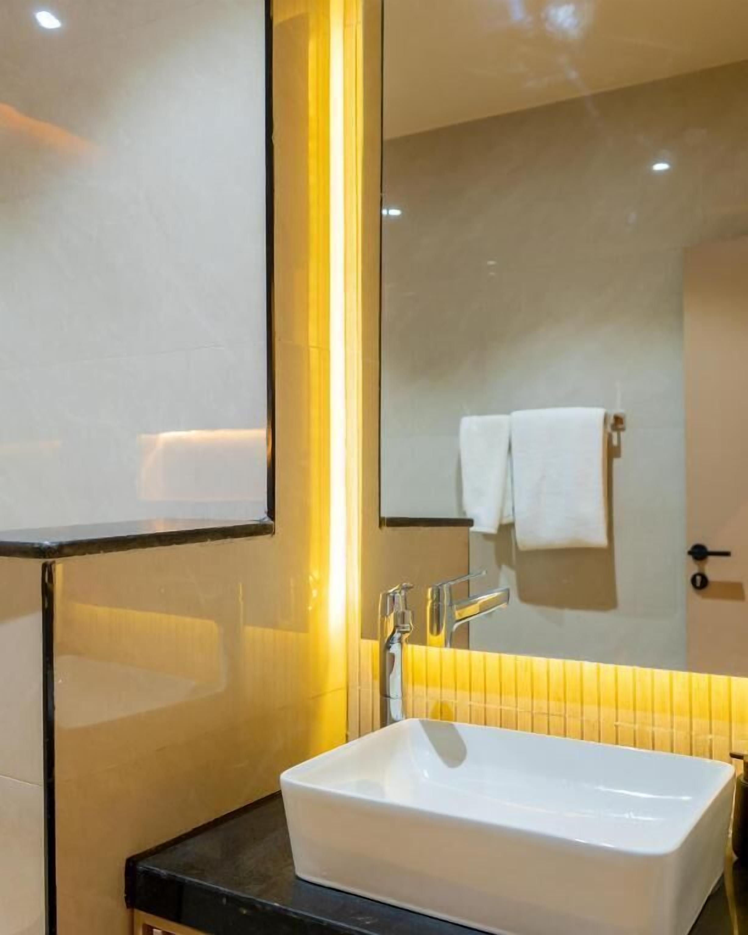 Un baño con un lavamanos blanco, un espejo y una toalla colgada en la pared.