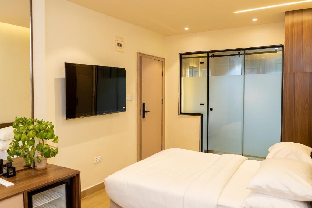 A hotel room with a bed, a television mounted on the wall, a sliding door closet, and a small table with a plant.