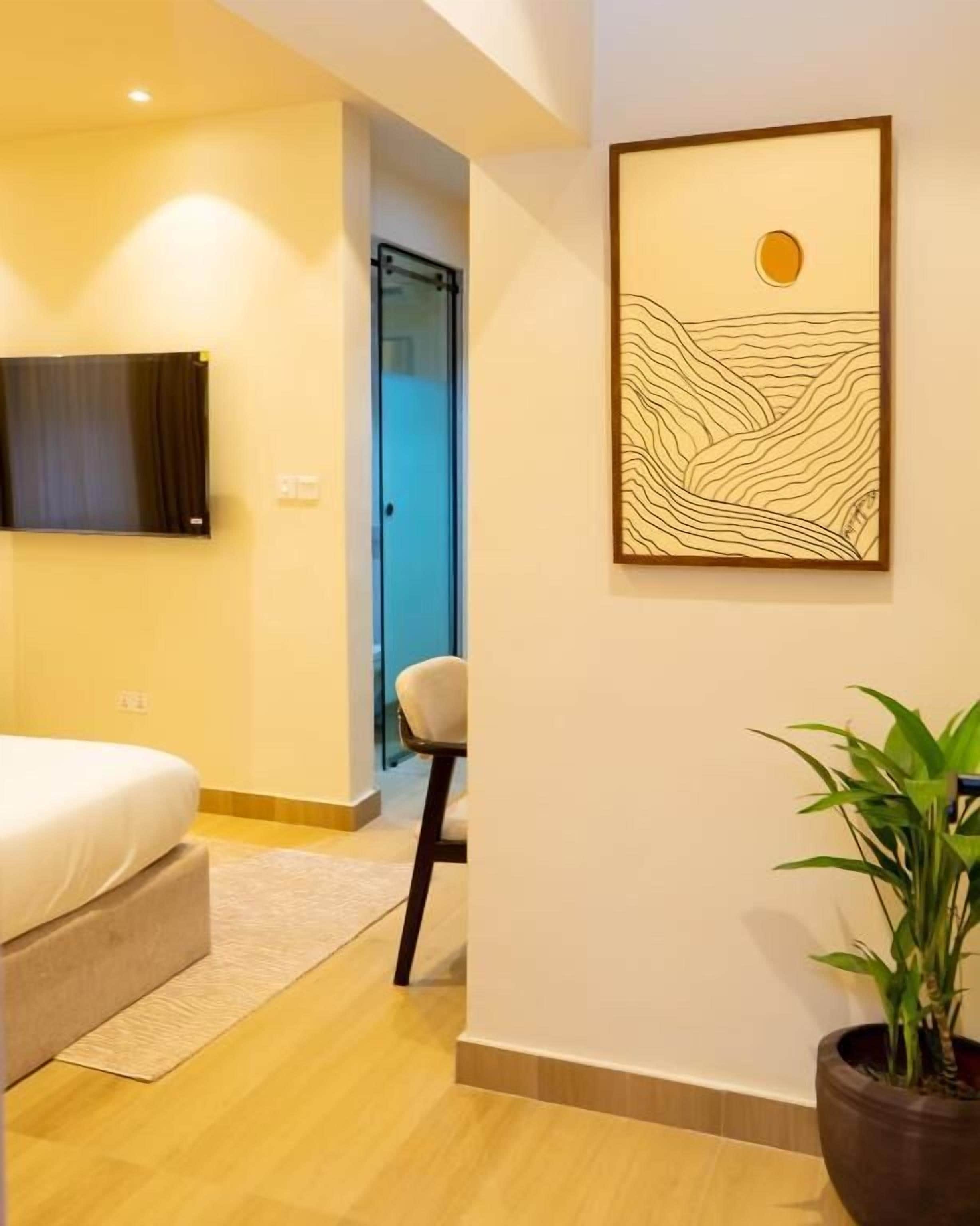 Un dormitorio moderno con una cama, una silla, una planta en maceta y una obra de arte colgada en la pared.
