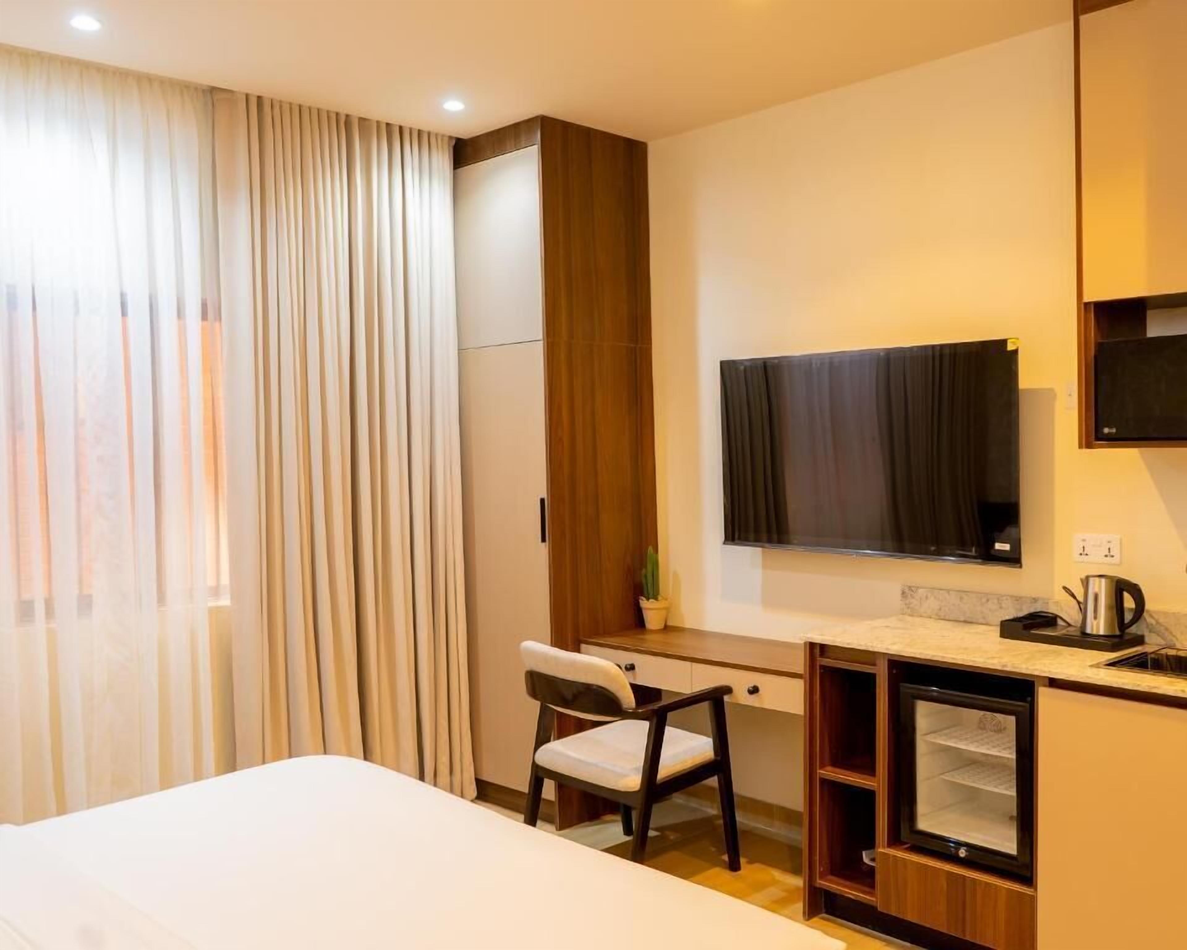 A hotel room with a bed, a desk, a chair, a television, and a kitchenette area.