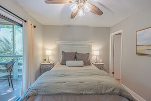 Ein Schlafzimmer mit einem Bett, zwei Nachttischen, einem Deckenventilator und einem Fenster mit Vorhängen.
