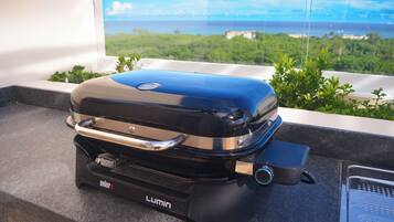 Una parrilla Weber Lumin en un balcón con vista al océano y follaje.