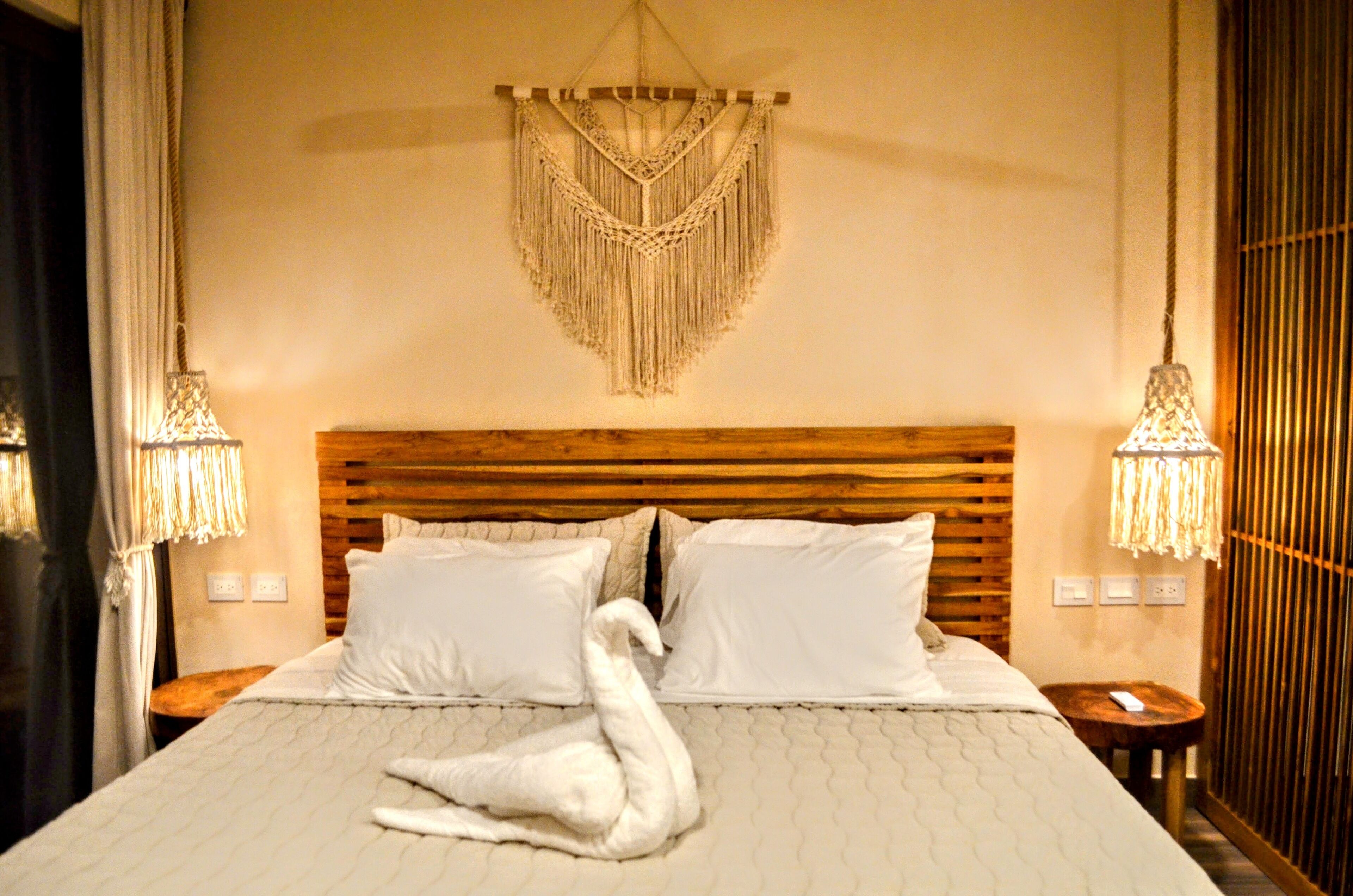 A bed with a macrame wall hanging, two bedside lamps, and a wooden headboard.