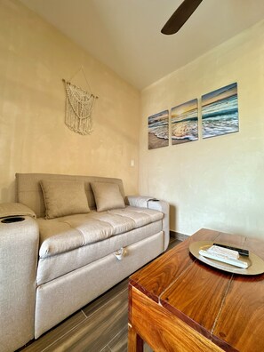 Una habitación con un sofá color beige, una mesa de madera y obras de arte colgadas en la pared.