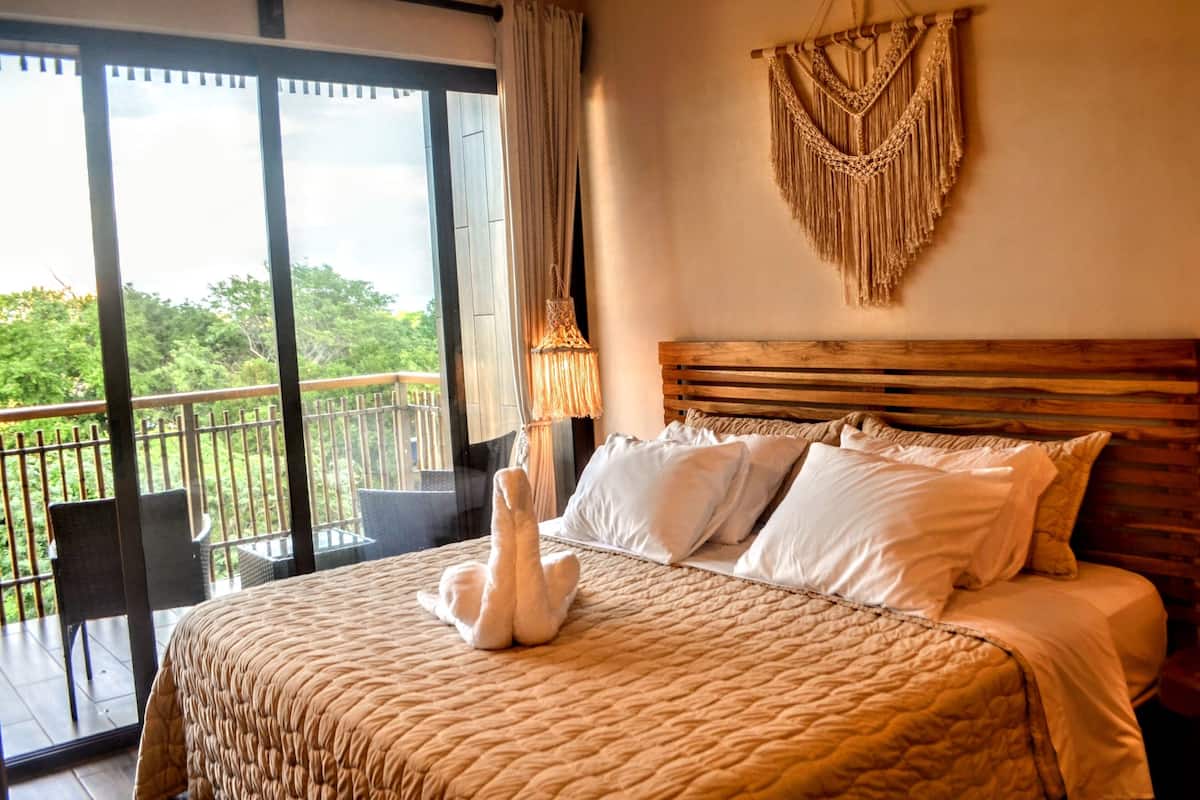 Een slaapkamer met een groot bed, een houten hoofdbord en een macramé wanddecoratie.
