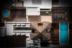 Un área de piscina exterior moderna con una gran fuente de agua, una estructura de techo de paja y una piscina separada.