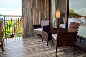 Een balkon met rieten stoelen, een houten vloer en uitzicht op groen.
