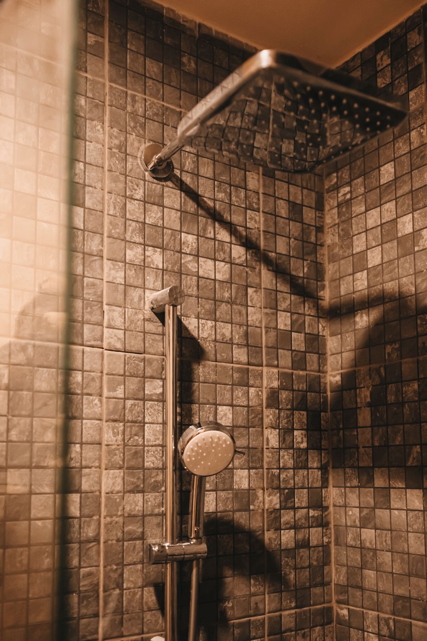 Een douche met een handdouche en een vaste douchekop, beide bevestigd aan een betegelde muur.