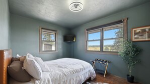 Quarto com cama, televisão, janela com vista e planta em vaso.