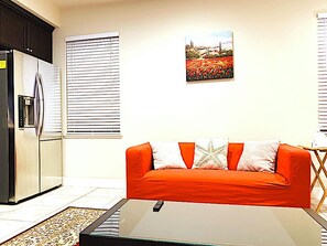 Ein Wohnzimmer mit einer Couch, einem Couchtisch, einem Kühlschrank und einem Bild an der Wand.