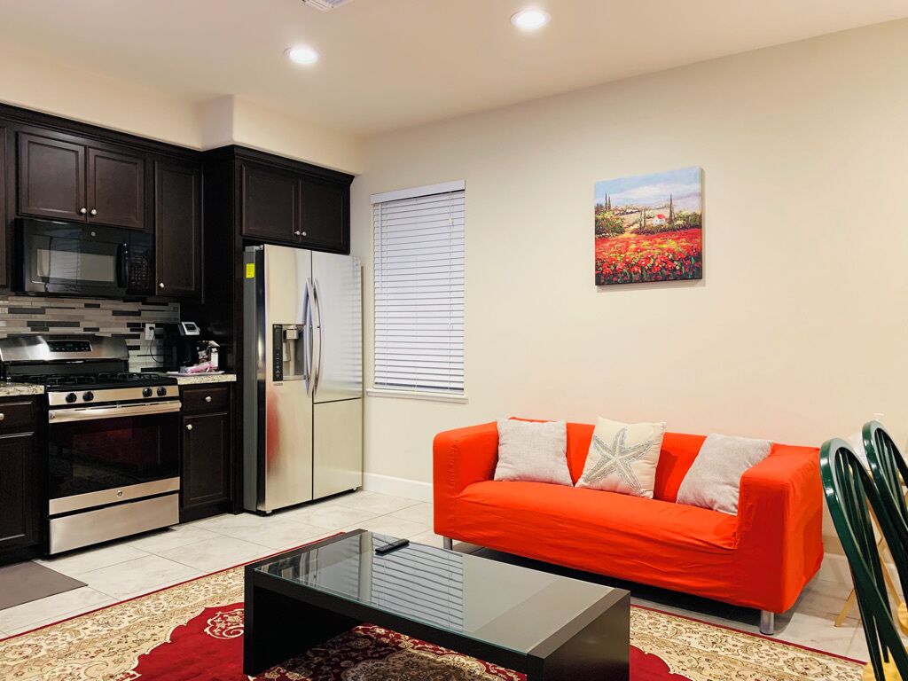 Una cocina moderna con armarios oscuros, un refrigerador y un microondas. Hay un sofá rojo con cojines blancos y un cuadro de flores en la pared.