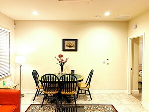 A dining area with a round table, four chairs, a vase with flowers, and a framed picture on the wall. - Brand new guest suite in beautiful locality (Mountain House)