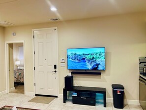 Ein Wohnzimmer mit an der Wand montiertem Fernseher, einer schwarzen Unterhaltungseinheit, einer Tür und einem Mülleimer.