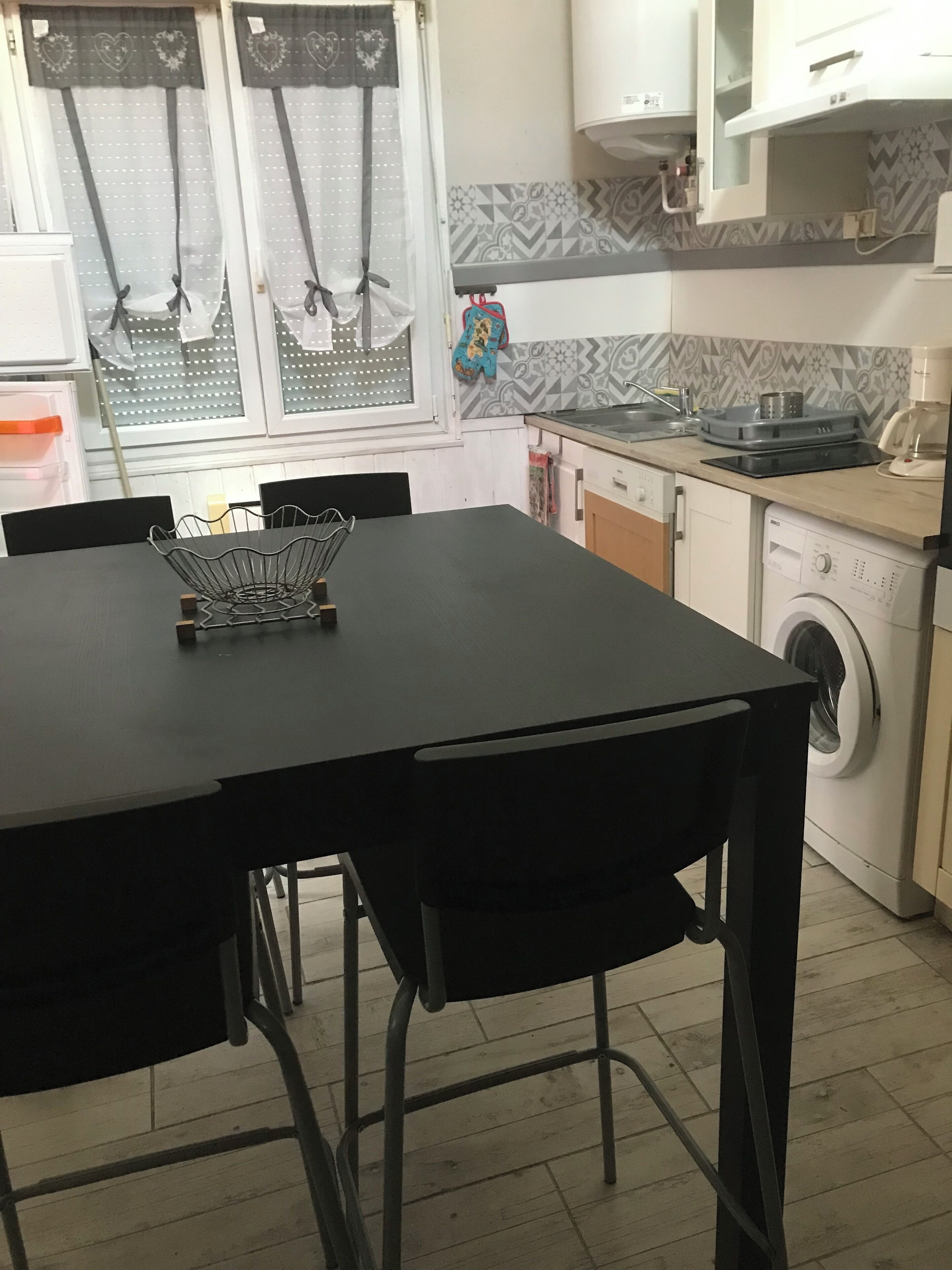 Une cuisine équipée d’une table à manger, de chaises, d’un lave-linge et d’une fenêtre avec des rideaux.