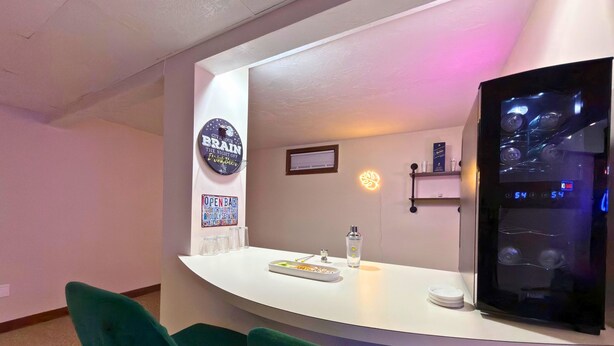 Eine Bar mit einer Theke, zwei grünen Stühlen, einem Kühlschrank und einem Neonzeichen.