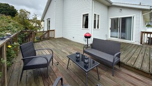 Eine überdachte Terrasse mit Gartenmöbeln, einem Grill und einer Schiebetür zu einem Schlafzimmer.