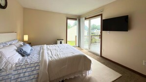 Ein Schlafzimmer mit Bett, Nachttisch, Lampe, Fernseher und einer Schiebetür zu einem Balkon.