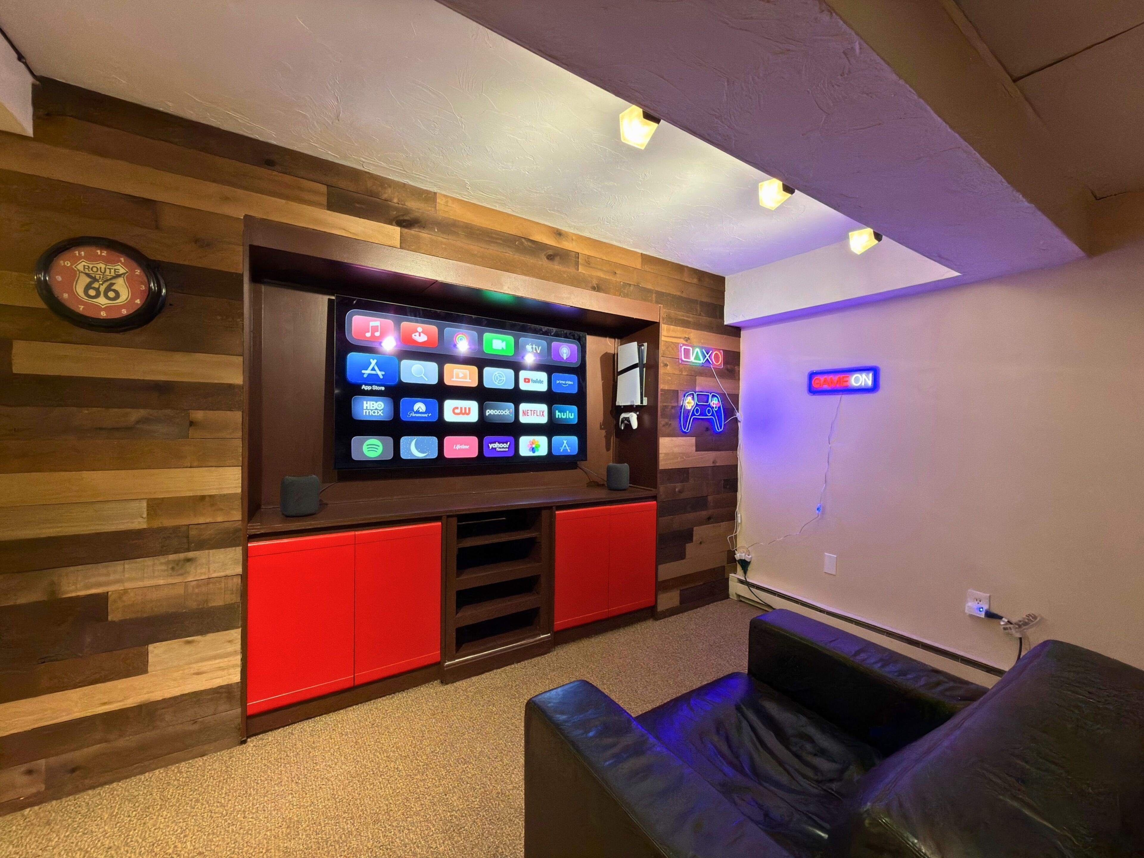 Een kamer met een wandgemonteerde televisie waarop verschillende streaming-apps worden weergegeven, een neonbord en een klok aan de muur.