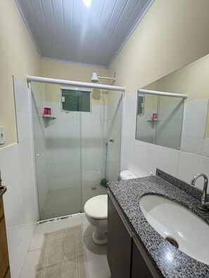 Ein Badezimmer mit Duschkabine, weißer Toilette, Waschtisch mit Granitplatte und Spiegel über dem Waschbecken.
