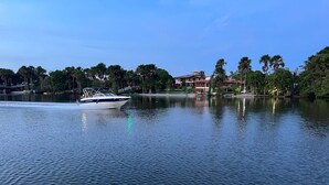 A calm lake with a boat in motion, surrounded by trees and buildings in the background. - Casa 40, Condomínio Lençóis Ville Residence (Barreirinhas)
