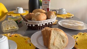 A table with various food items, including bread, a basket, and a plate with a white cloth napkin. - Casa 40, Condomínio Lençóis Ville Residence (Barreirinhas)