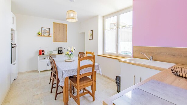 A modern kitchen with a dining area, featuring a wooden table, chairs, and a hanging light fixture.