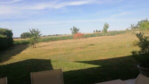 An outdoor seating area with a table and chairs, overlooking a grassy field with trees and a fence in the distance.