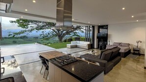 A modern kitchen with a central island, a dining area with a sofa, and a large window overlooking a scenic landscape. - LoftMerak sunsets, Jacuzzi, terrace, privacy, wifi (Pereria)