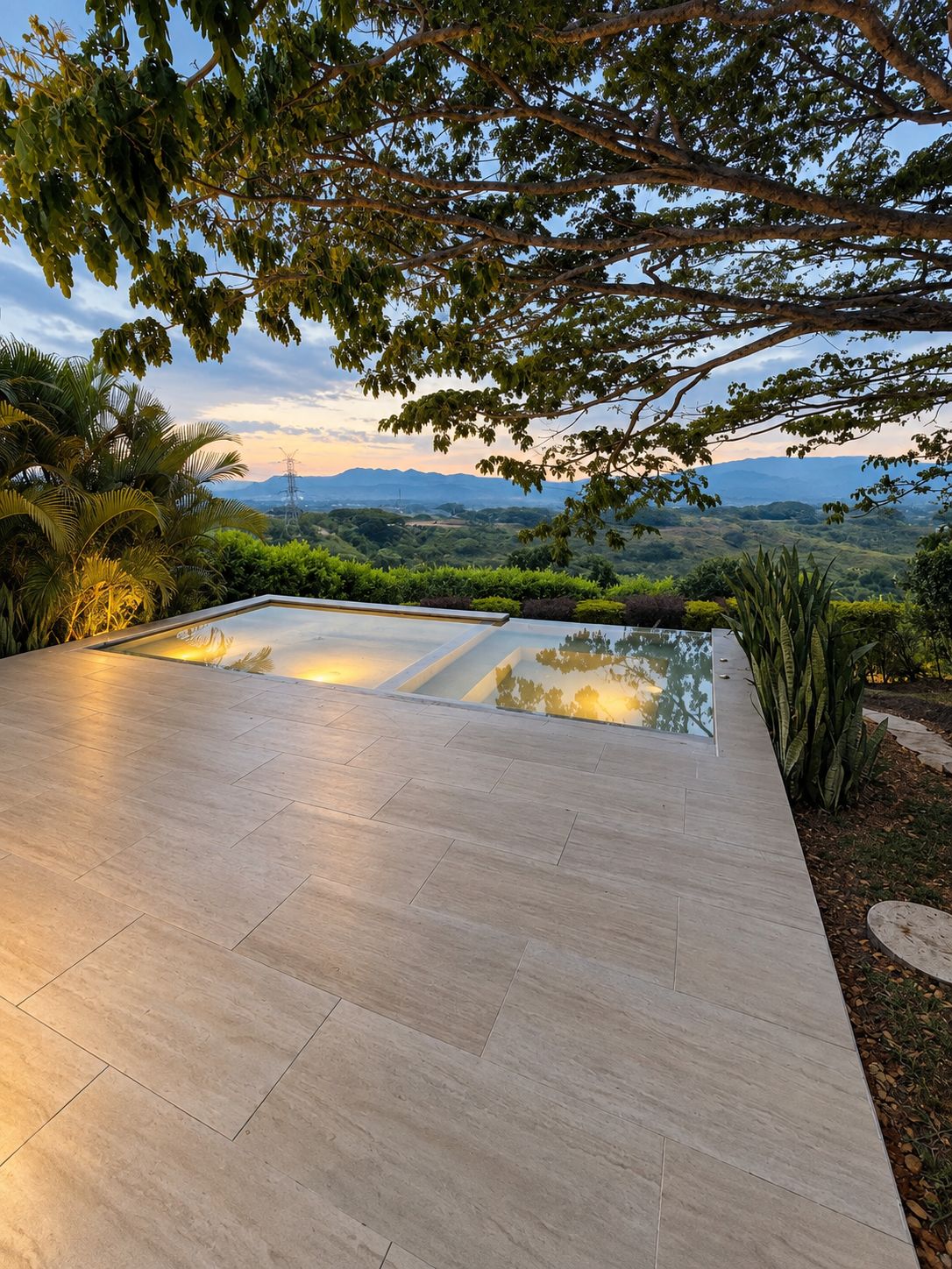 A modern outdoor patio with a reflective pool, surrounded by lush greenery and overlooking a scenic landscape.