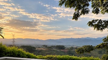 Uma pessoa segurando uma xícara de café com vista panorâmica para montanhas e céu claro.