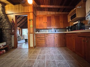 A rustic kitchen with wooden cabinets, a stone wall, and a tiled floor. - China Lake Waterfront Getaway at relaxing Camp Loonsong (China)