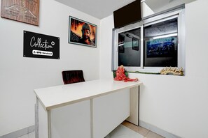 A room with a white desk, a window with a view, and a Buddha painting on the wall. - Ollection O Sector 95B Gurgaon (Gurugram)