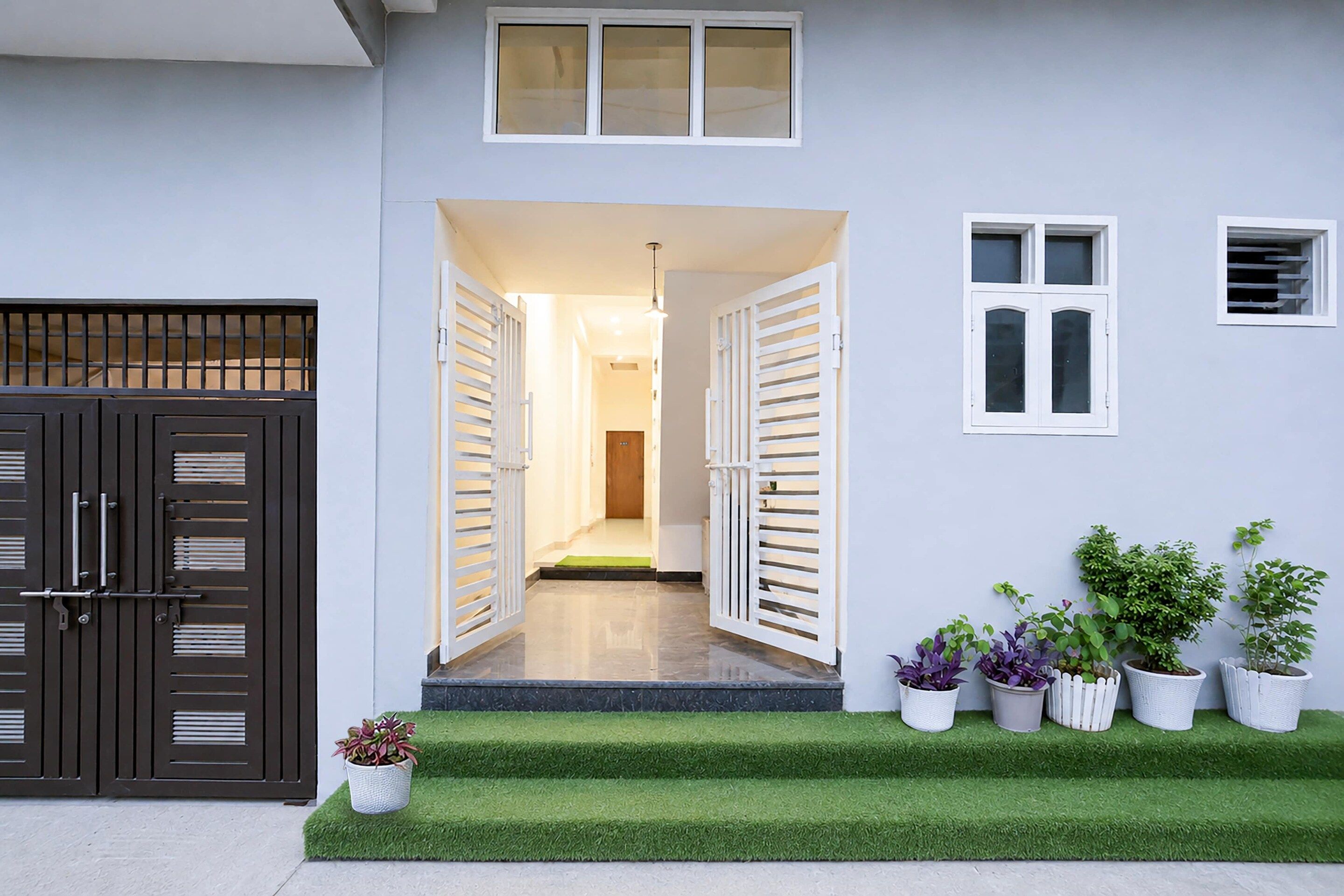 Una entrada residencial con un doble puerta, un pasillo y un pequeño porche con plantas en macetas.