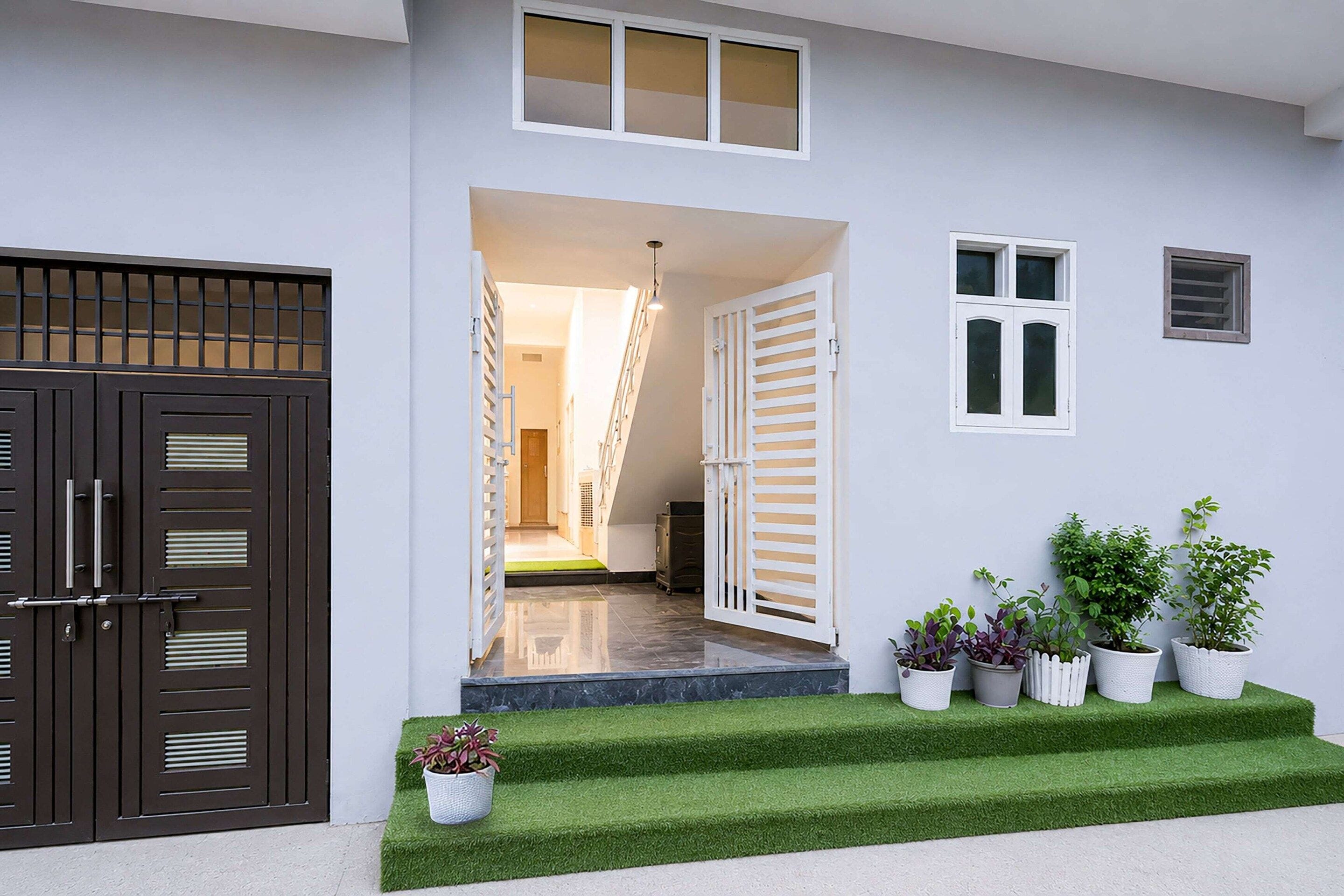 A house entrance with a dark brown gate, a white door, and a staircase leading to a hallway.
